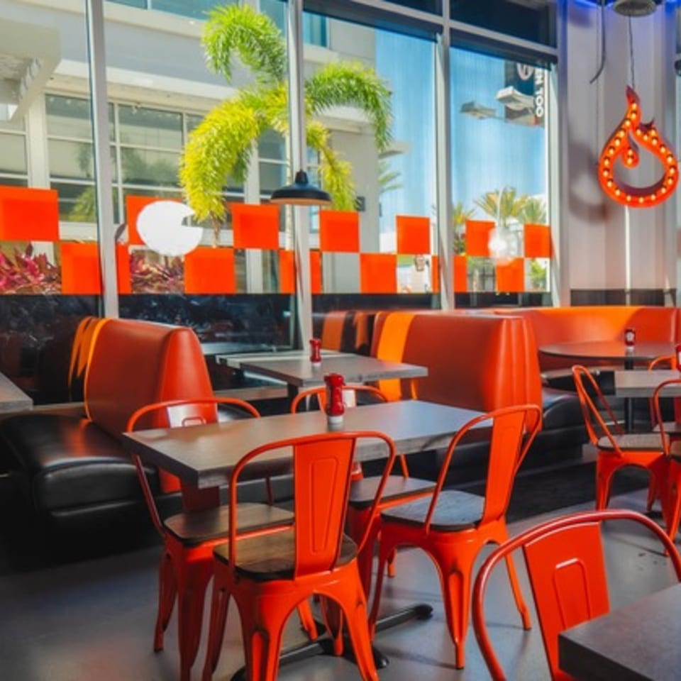 Interior of BurgerTen and ChickenToo with orange booths, chairs, and tables, and a flame-shaped neon sign.