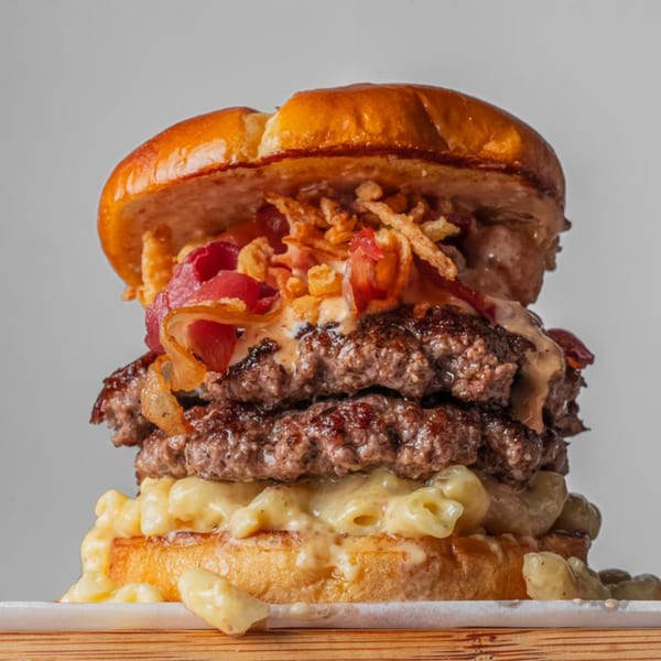 A BurgerTen burger with two patties, mac and cheese, bacon, crispy onions, and sauce.