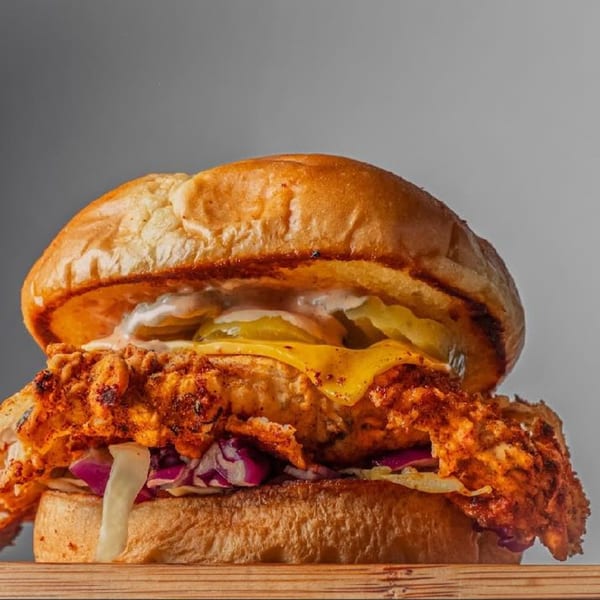 A crispy fried chicken sandwich with cheese, pickles, and red cabbage on a bun.