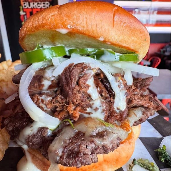 A BurgerTen burger with pulled beef, melted cheese, onions, and green peppers on a bun.