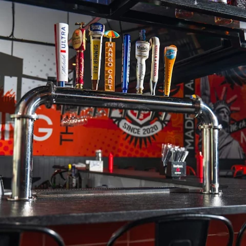 Beer taps with various brand handles line a bar counter at BurgerTen and ChickenToo.