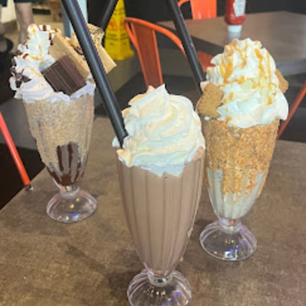 Three BurgerTen and ChickenToo milkshakes, topped with whipped cream, chocolate, and caramel, on a table.
