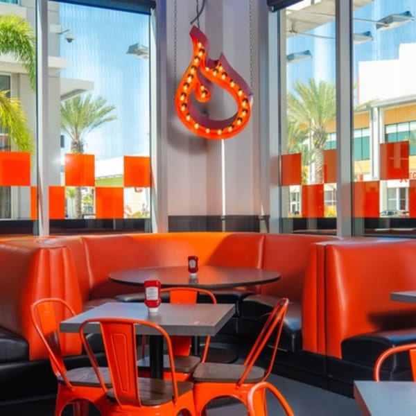 BurgerTen and ChickenToo's vibrant dining area with orange booths, tables, and a flame-shaped neon sign.