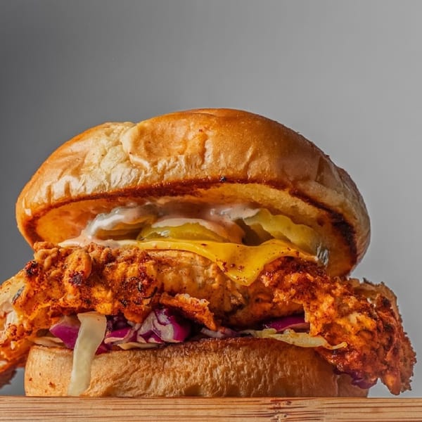 Close-up of a BurgerTen and ChickenToo fried chicken sandwich with cheese, pickles, and slaw.
