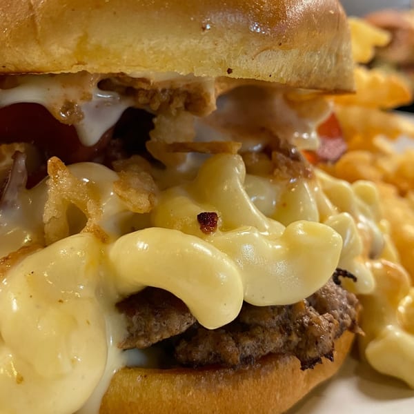 Close-up of a BurgerTen burger with mac and cheese, crispy onions, and fries.