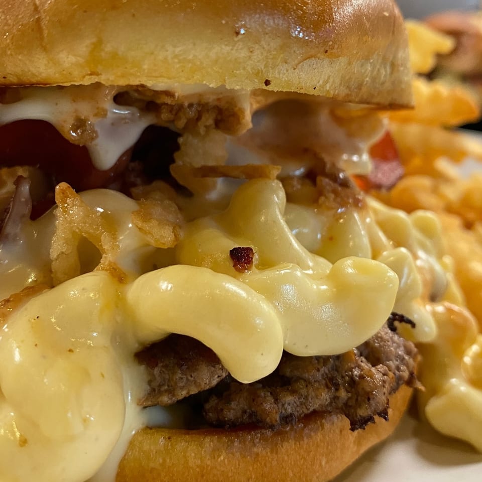 Close-up of a BurgerTen burger with mac and cheese, crispy onions, and fries.