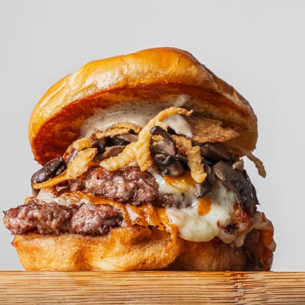 A BurgerTen mushroom burger with melted cheese, crispy onions, and creamy sauce on a bun.