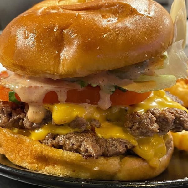 Close-up of a BurgerTen burger with melted cheese, tomato, lettuce, and special sauce on a brioche bun.